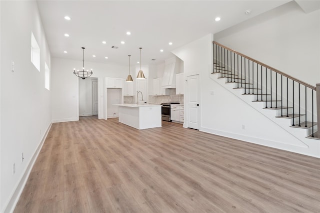 unfurnished living room featuring a notable chandelier, a sink, light wood-style flooring, and stairs