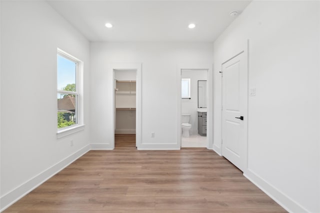 unfurnished bedroom featuring connected bathroom, recessed lighting, baseboards, light wood-type flooring, and a walk in closet