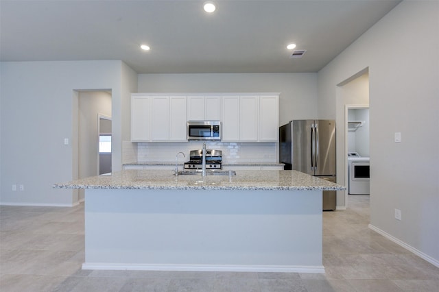 kitchen with stainless steel appliances, decorative backsplash, light stone countertops, washer / clothes dryer, and an island with sink