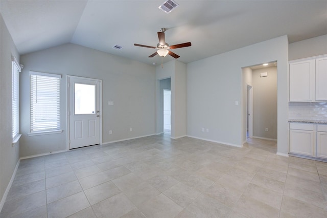 unfurnished living room with ceiling fan, visible vents, vaulted ceiling, and baseboards