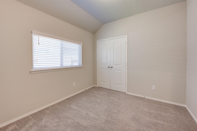 unfurnished bedroom with a closet, light colored carpet, vaulted ceiling, and baseboards