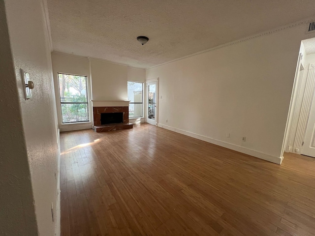 unfurnished living room with a textured ceiling, hardwood / wood-style flooring, a fireplace, baseboards, and ornamental molding