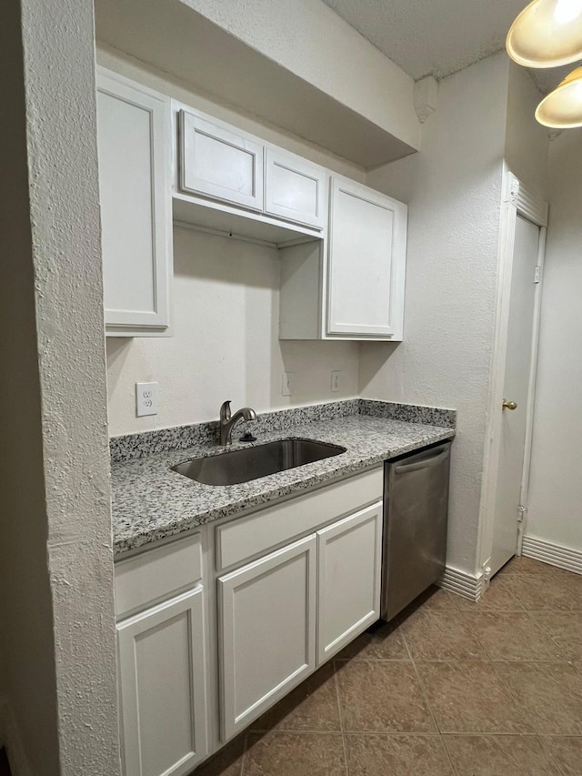 kitchen featuring light stone counters, white cabinets, a sink, dishwasher, and dark tile patterned floors