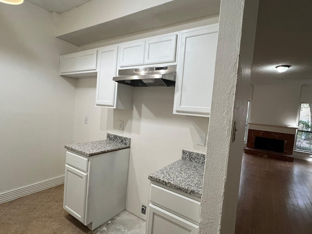 kitchen featuring light stone counters, white cabinets, under cabinet range hood, and baseboards