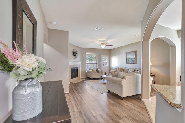 living room with visible vents, ceiling fan, light wood-type flooring, baseboards, and a tile fireplace