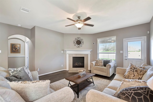 living room with baseboards, visible vents, a ceiling fan, a tiled fireplace, and wood finished floors