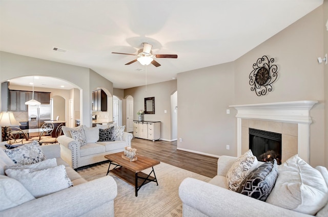 living area featuring visible vents, arched walkways, a ceiling fan, light wood-style floors, and a fireplace