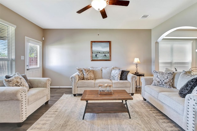 living room with a ceiling fan, visible vents, baseboards, and wood finished floors