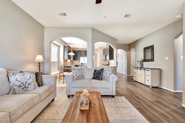 living area featuring arched walkways, visible vents, dark wood finished floors, and baseboards