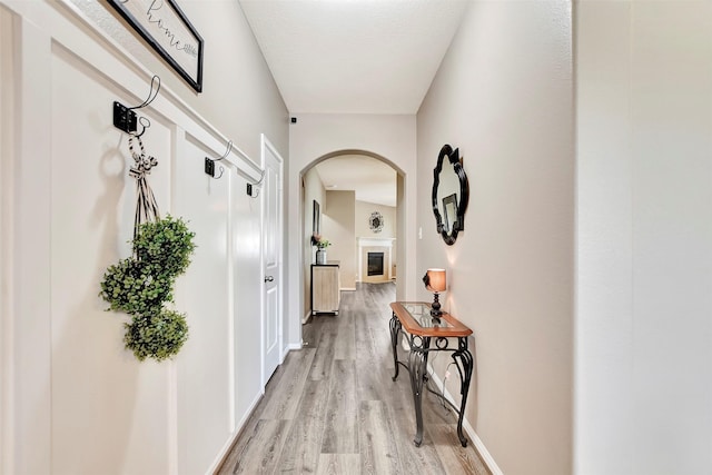 corridor with arched walkways, light wood-style flooring, and baseboards