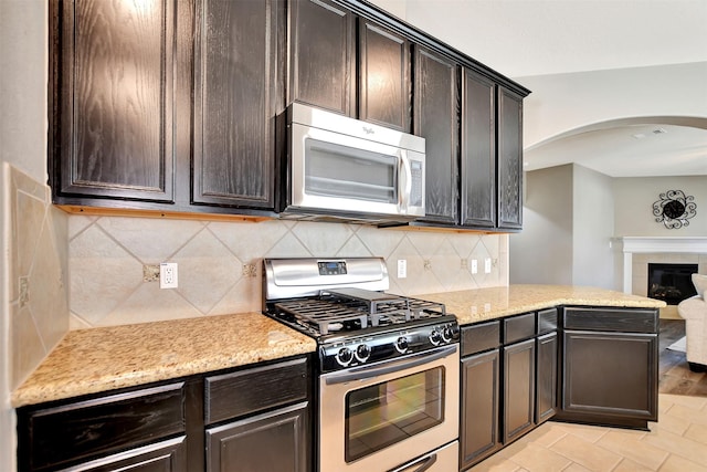 kitchen featuring appliances with stainless steel finishes, a tile fireplace, dark brown cabinetry, and decorative backsplash