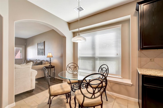 dining space featuring arched walkways, light tile patterned floors, visible vents, and baseboards