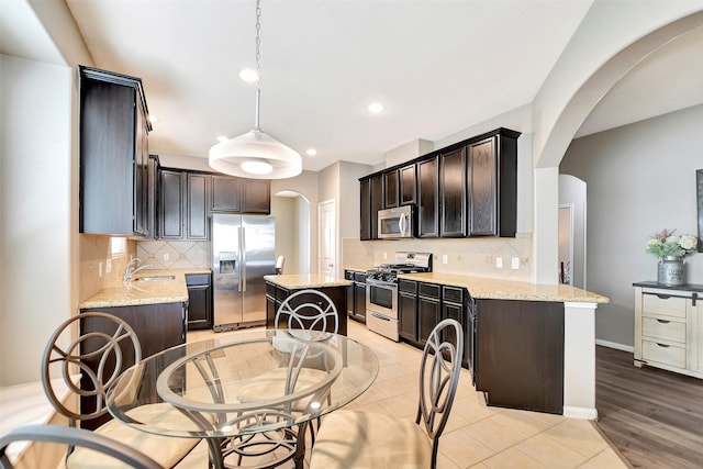 kitchen with appliances with stainless steel finishes, arched walkways, light stone counters, and tasteful backsplash