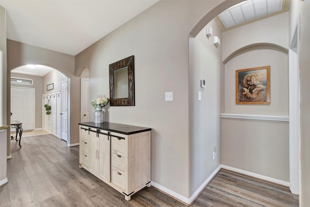 hallway with arched walkways, baseboards, visible vents, and light wood finished floors