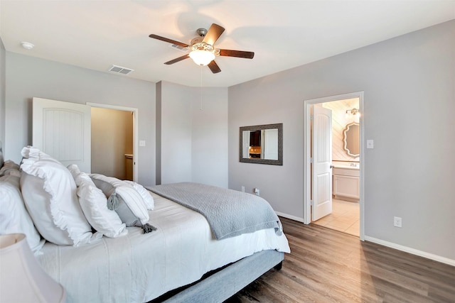 bedroom with baseboards, visible vents, a ceiling fan, ensuite bath, and wood finished floors