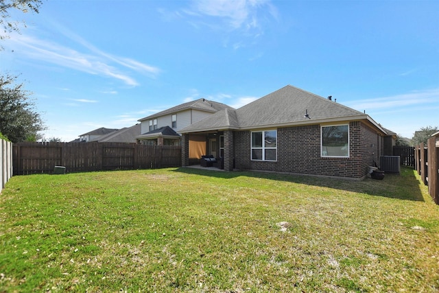 back of property featuring a fenced backyard, central air condition unit, brick siding, a shingled roof, and a lawn