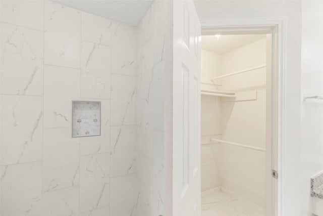 full bathroom with marble finish floor, a spacious closet, walk in shower, and a textured ceiling