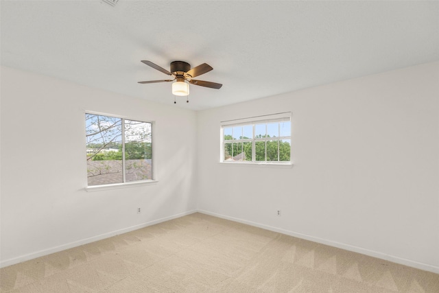 spare room featuring light carpet, baseboards, and a ceiling fan