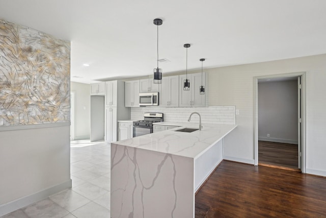 kitchen featuring light stone counters, a peninsula, a sink, appliances with stainless steel finishes, and backsplash