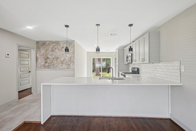 kitchen featuring a peninsula, hanging light fixtures, stainless steel appliances, light countertops, and a sink