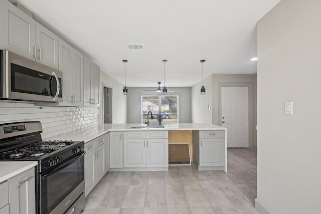 kitchen with a peninsula, a sink, light countertops, stainless steel microwave, and gas range