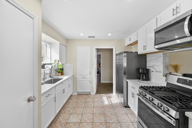 kitchen with white cabinetry, stainless steel appliances, a sink, and light countertops