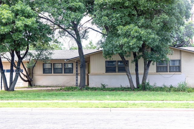 view of front facade with roof with shingles, a front lawn, board and batten siding, and brick siding