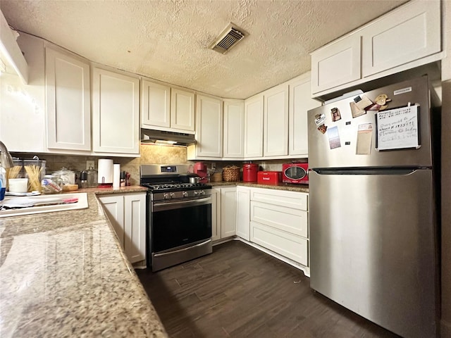 kitchen with under cabinet range hood, stainless steel appliances, dark wood-style flooring, white cabinetry, and visible vents