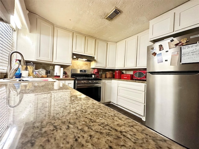 kitchen with under cabinet range hood, stainless steel appliances, a sink, visible vents, and white cabinets