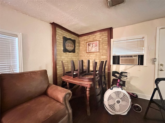 interior space with baseboards, visible vents, brick wall, wood finished floors, and a textured ceiling