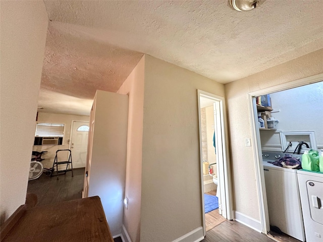 hallway featuring a textured ceiling, a textured wall, dark wood-style flooring, baseboards, and washer and dryer