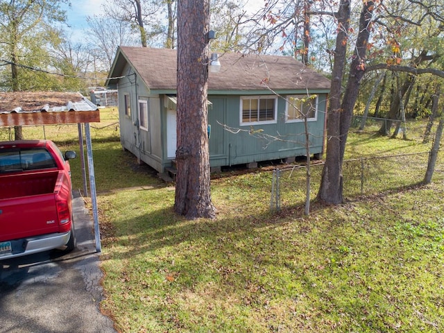 view of side of property with a carport, roof with shingles, a yard, and fence