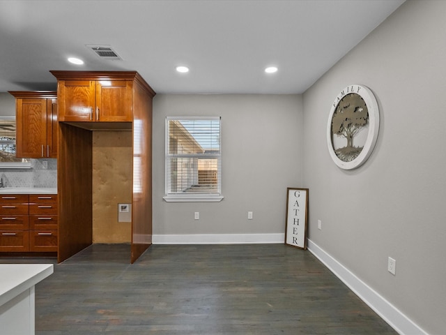 interior space featuring dark wood-type flooring, brown cabinetry, light countertops, decorative backsplash, and baseboards