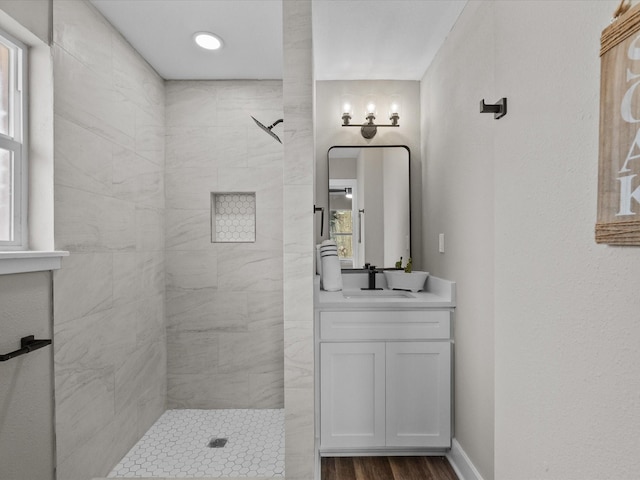 full bath with vanity, plenty of natural light, wood finished floors, and tiled shower