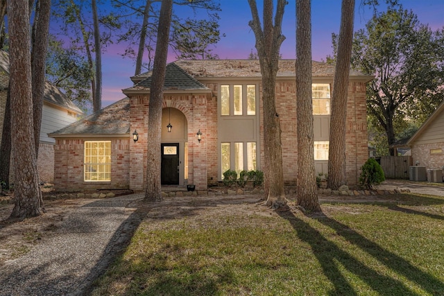 view of front facade with brick siding, roof with shingles, fence, central air condition unit, and a front yard