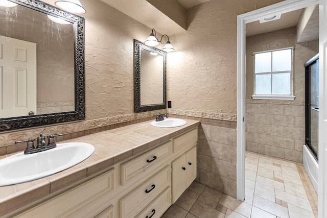 bathroom featuring a textured wall, a wainscoted wall, a sink, and tile walls