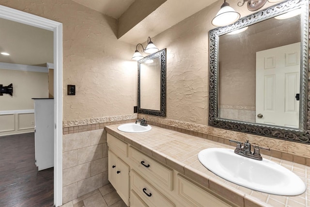 bathroom with a textured wall, double vanity, wainscoting, and a sink