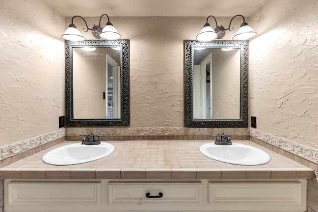 full bath with double vanity, a sink, and a textured wall