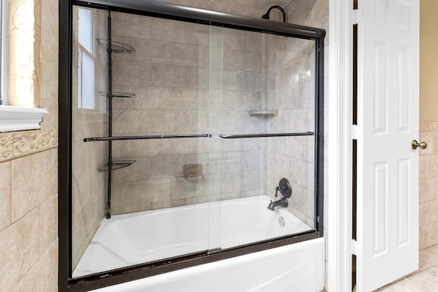 full bath featuring combined bath / shower with glass door and tile walls