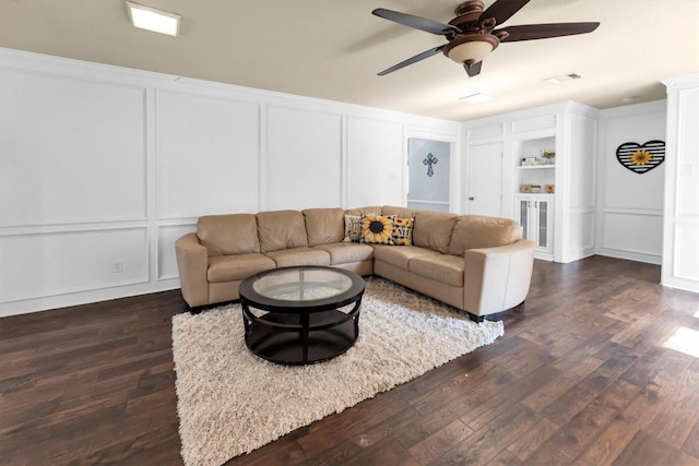 living room with a ceiling fan, dark wood finished floors, visible vents, and a decorative wall