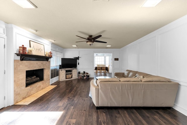 living room with dark wood finished floors, visible vents, a decorative wall, a ceiling fan, and a tile fireplace