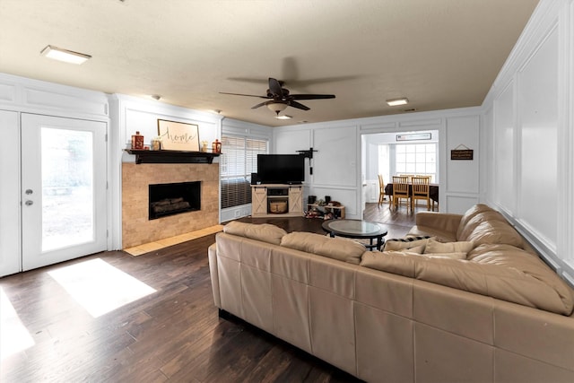 living room featuring dark wood-style floors, a decorative wall, a tiled fireplace, and a ceiling fan