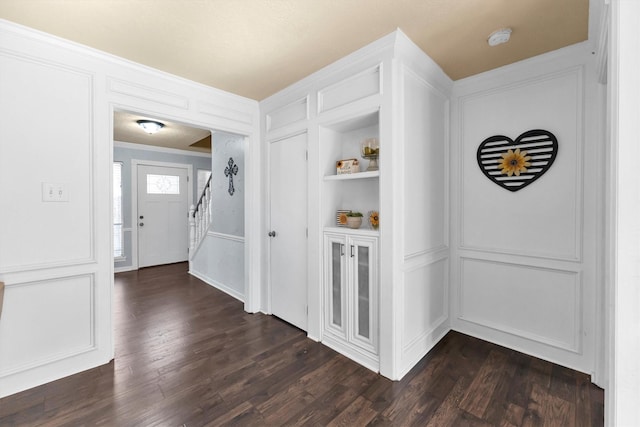 corridor featuring dark wood-style floors, crown molding, a decorative wall, and stairway