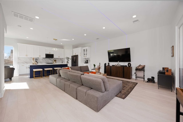 living room with light wood-type flooring, visible vents, and recessed lighting