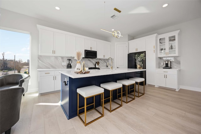 kitchen with light wood finished floors, light countertops, white cabinets, black appliances, and a kitchen breakfast bar