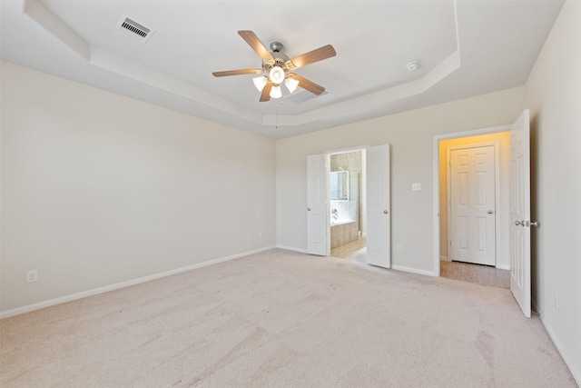 unfurnished bedroom featuring a tray ceiling, visible vents, ensuite bathroom, light carpet, and baseboards