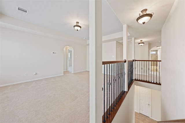 hall featuring arched walkways, carpet floors, visible vents, and baseboards