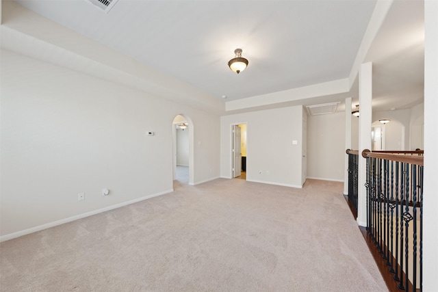 unfurnished room with arched walkways, light colored carpet, baseboards, a tray ceiling, and attic access