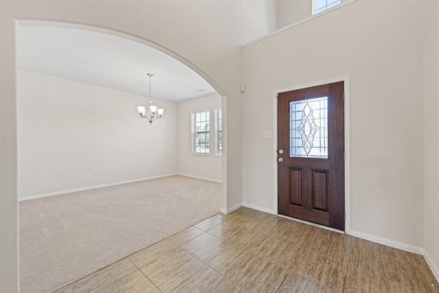 entryway featuring an inviting chandelier, baseboards, arched walkways, and carpet flooring