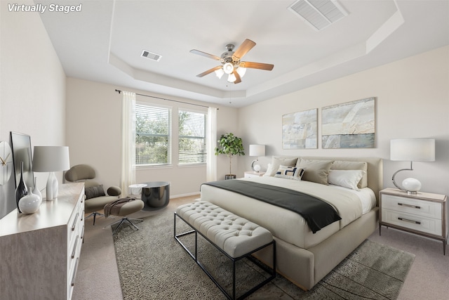 carpeted bedroom featuring visible vents, a tray ceiling, ceiling fan, and baseboards